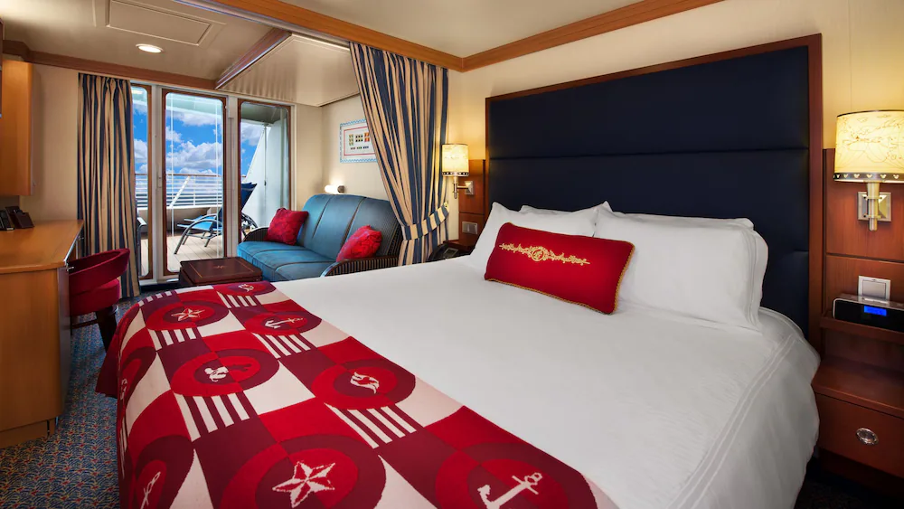 A stateroom with a bed, couch, coffee table and a deck with deck chairs