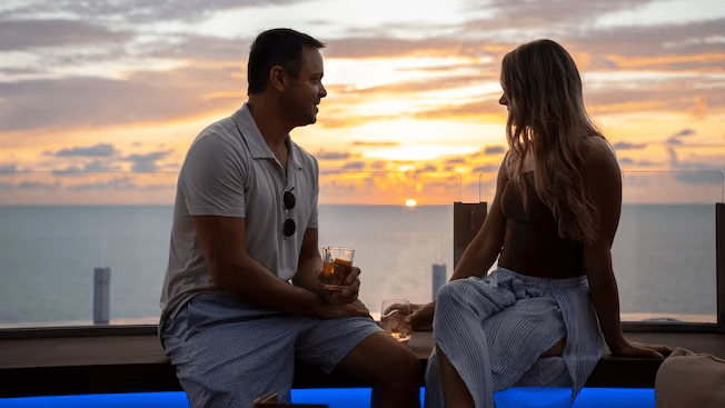 A couple enjoying beverages and the sunset on an outdoor bench at Infinity Bar on the Disney Adventure