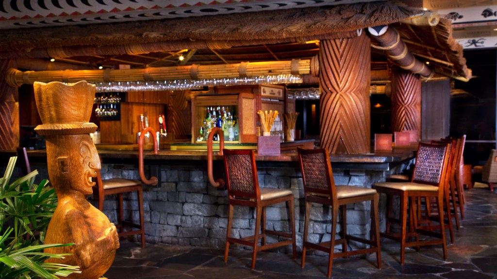 Tiki sculpture and a bar with wicker-back stool-chairs