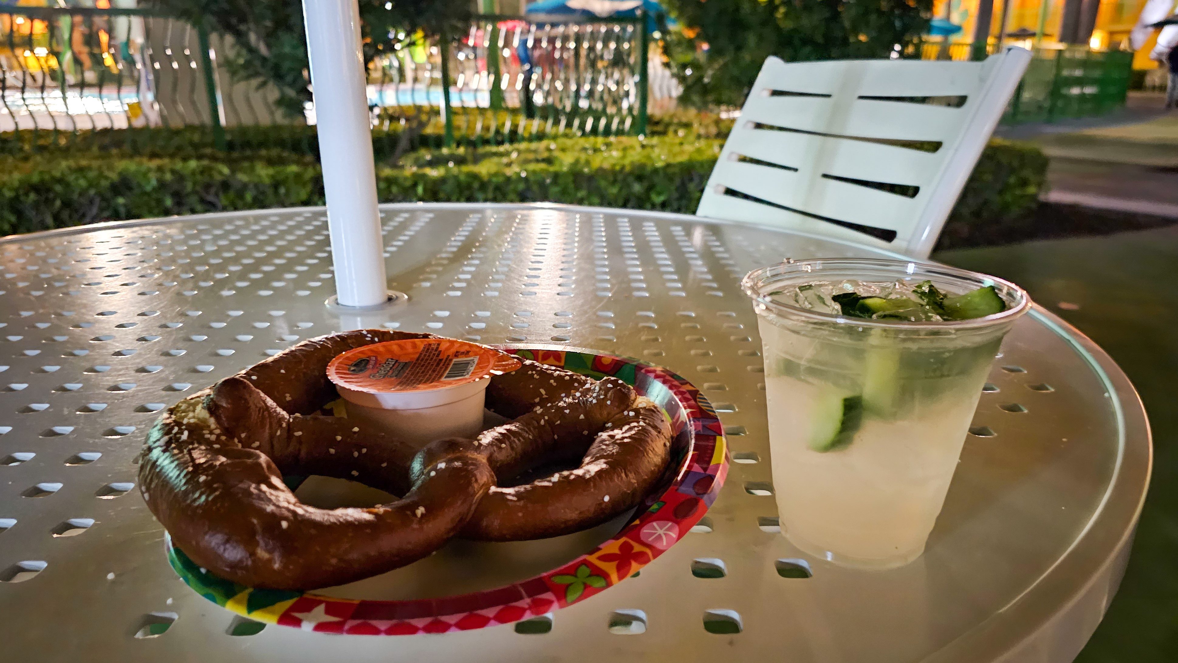 A pretzel with a cocktail on an outdoor table at night
